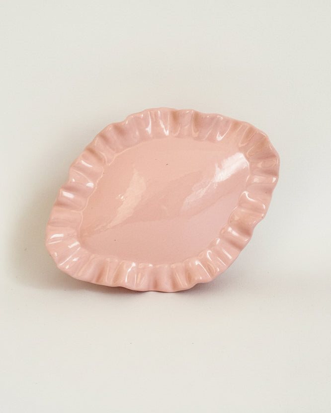 Pink ceramic plate with scalloped edge on a light gray background