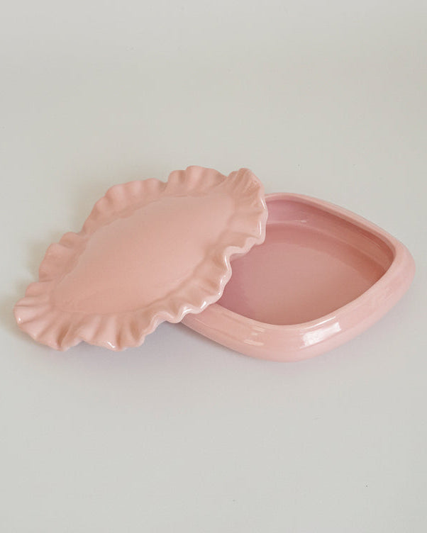 Pink ceramic dish with scalloped edge on a light gray background