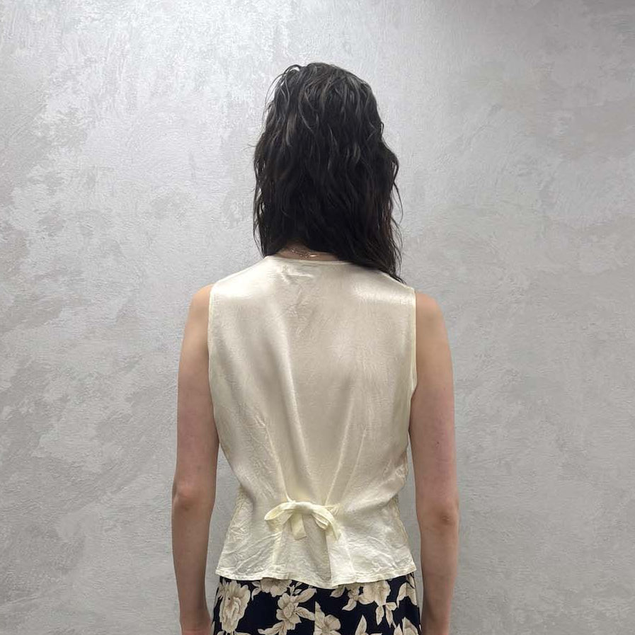 Person wearing a white sleeveless top with a tie in the back and floral skirt standing against a plain wall.