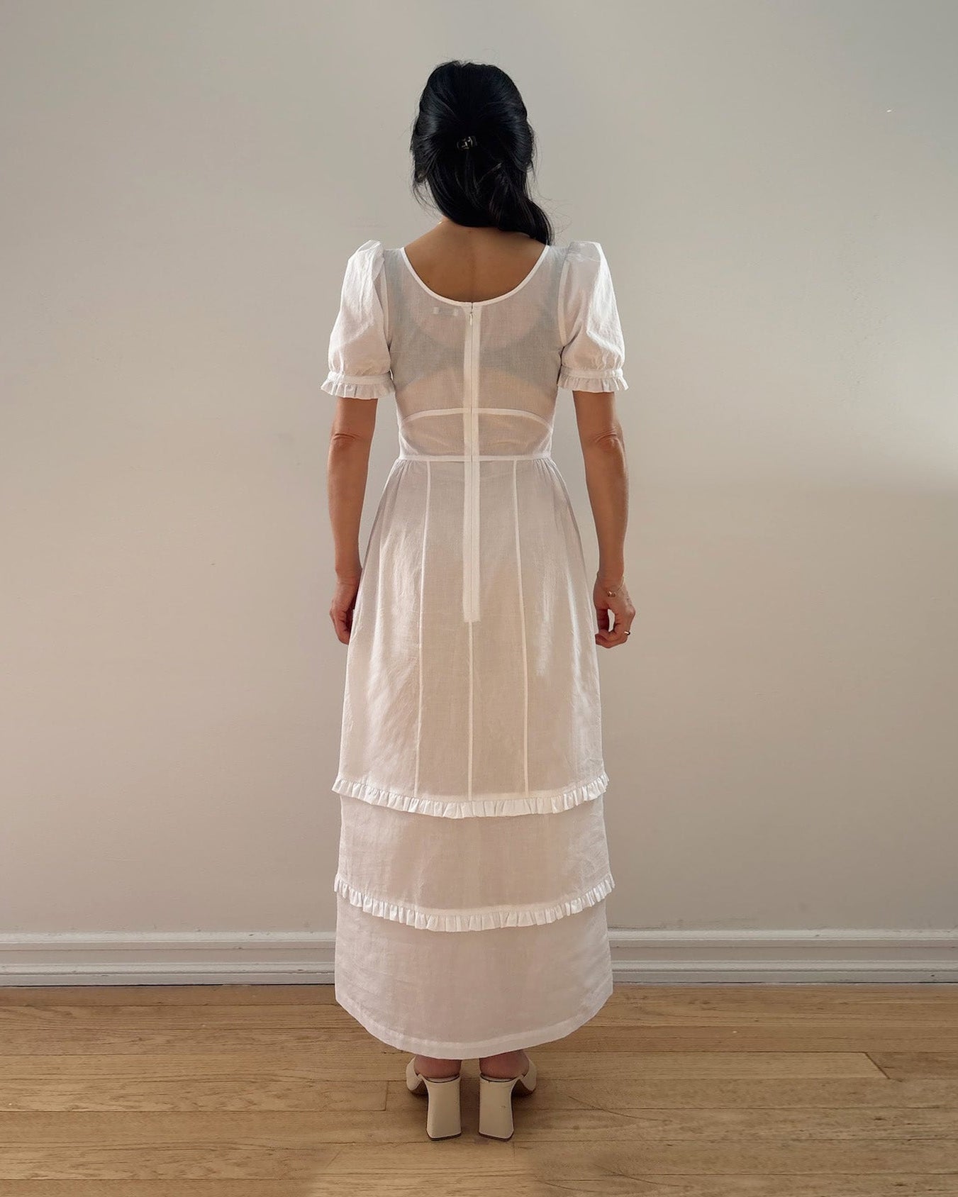 Person wearing a white vintage-style dress standing against a plain wall.