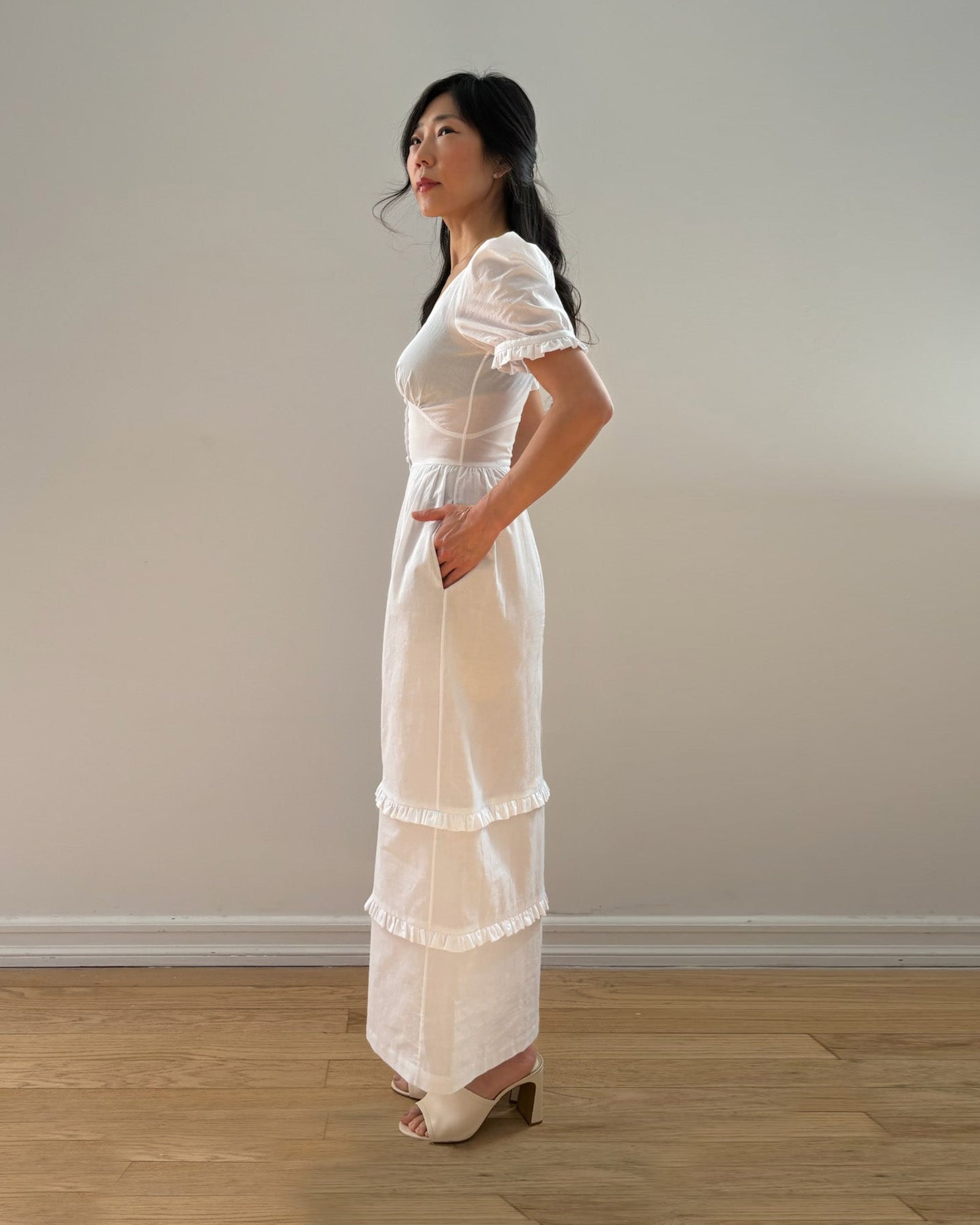 Woman wearing a white dress standing against a plain wall.